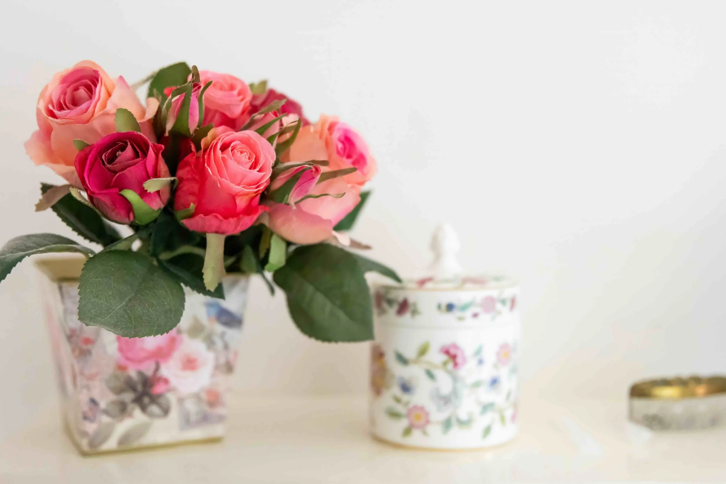 Ornaments on a white shelf. Roses in a floral ase, a floral ceramic jar with lid and a crystal trinket box with brass lid