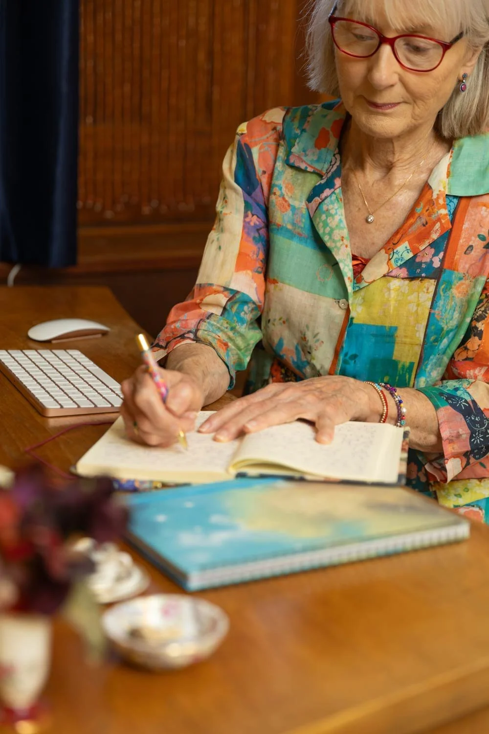 Older women sitting writing in her journal beside the computer.