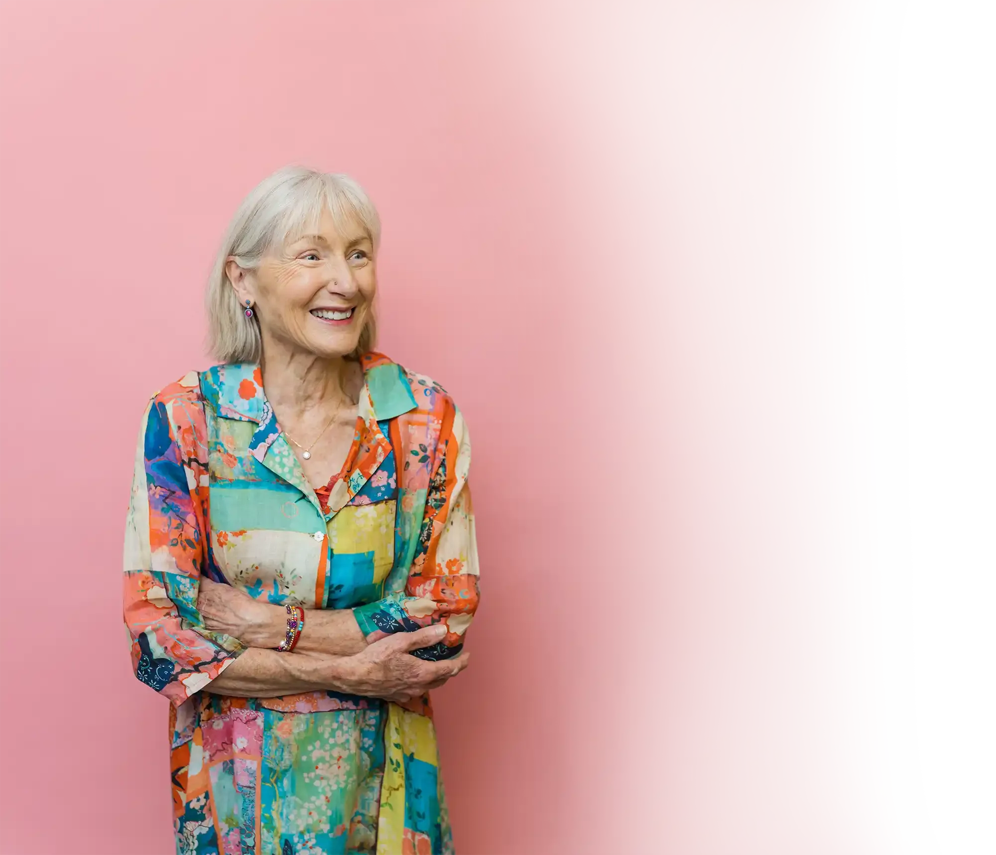 Penelope Lane, clinical psychologist, mindfulness teacher & ageing coach - wearing a colorful patchwork dress, smiling and crossing her arms, standing against a pink background.