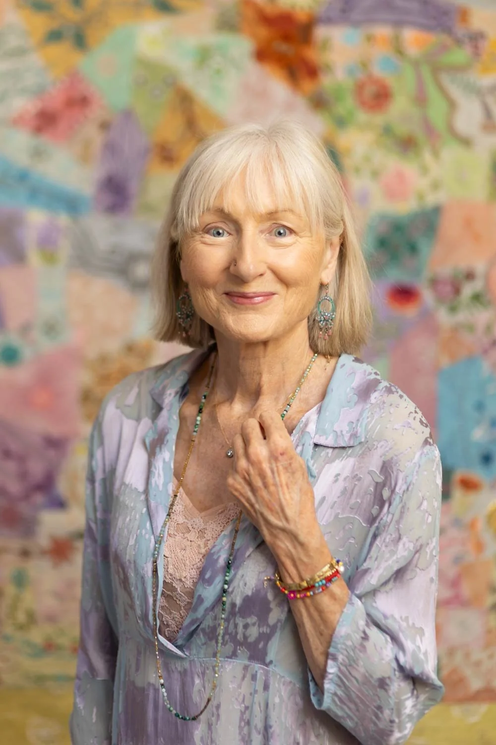 Penelope Lane, clinical psychologist, mindfulness teacher & ageing coach, smiling, wearing colorful jewelry and a pastel-colored blouse, standing in front of a vibrant, quilted background.