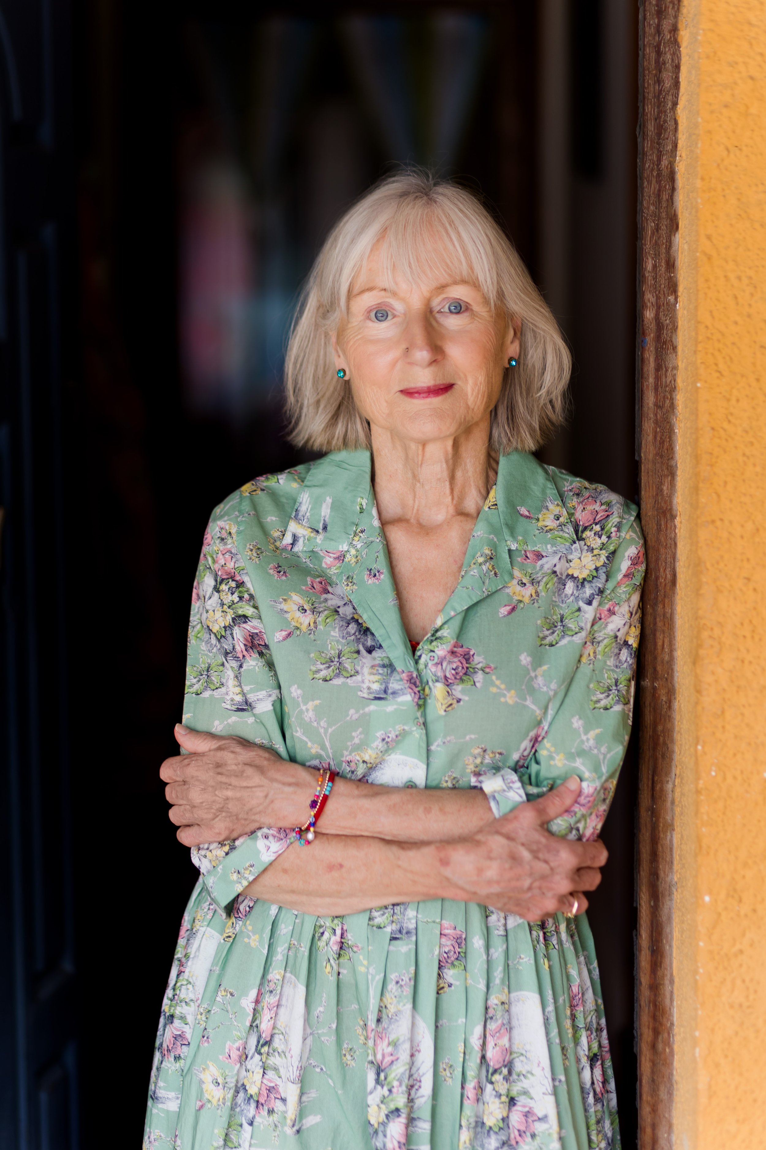 Older woman standing in a doorway with a floral green dress staring pensively into the distance