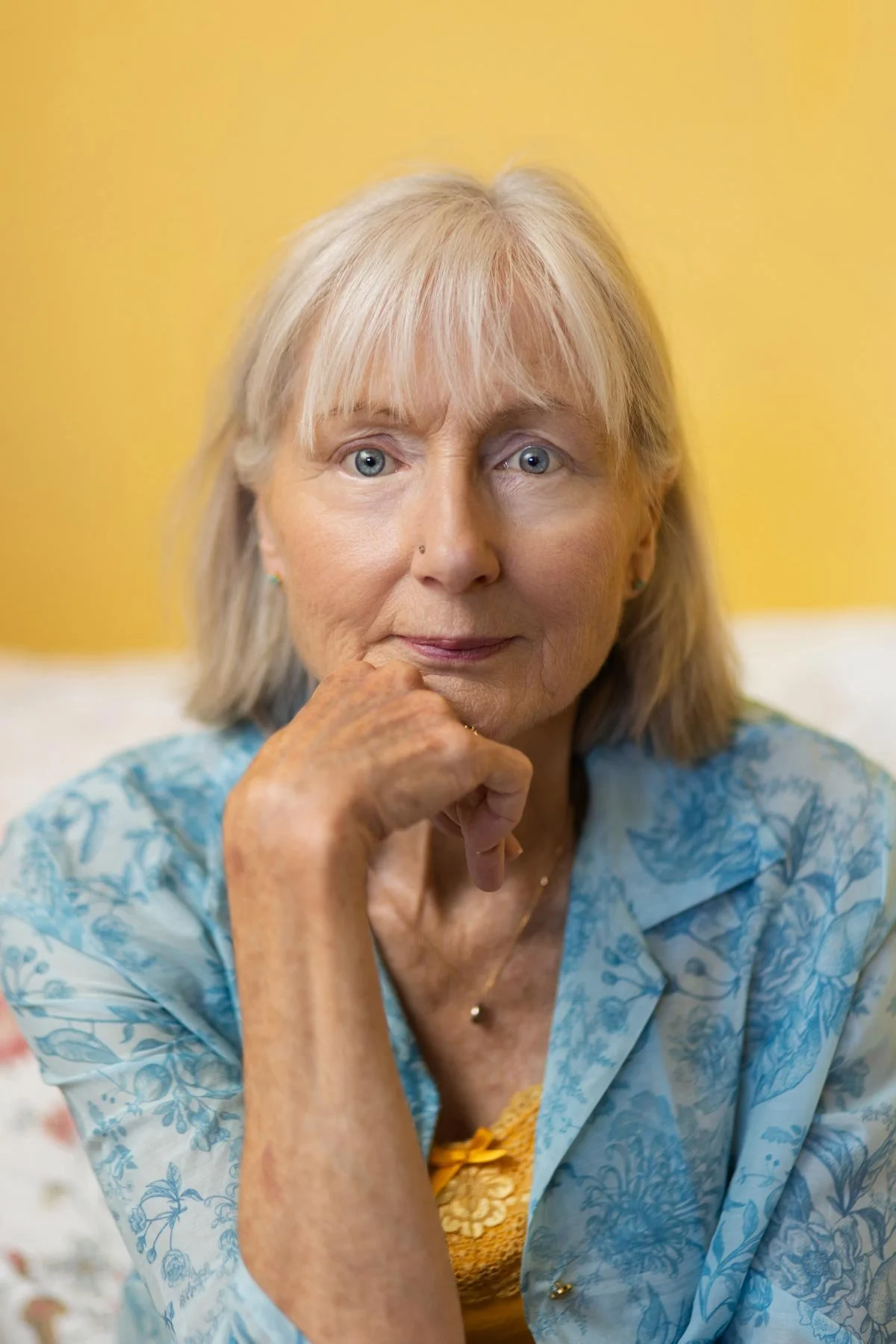Penelope Lane, healthy ageing & lifestyle coach, wearing a floral blue top, with hand on face, yellow background.