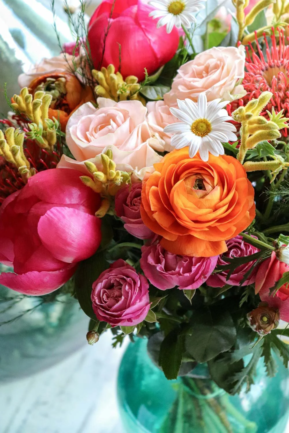 Bouquet of bright pink and orange flowers in a green glass vase.