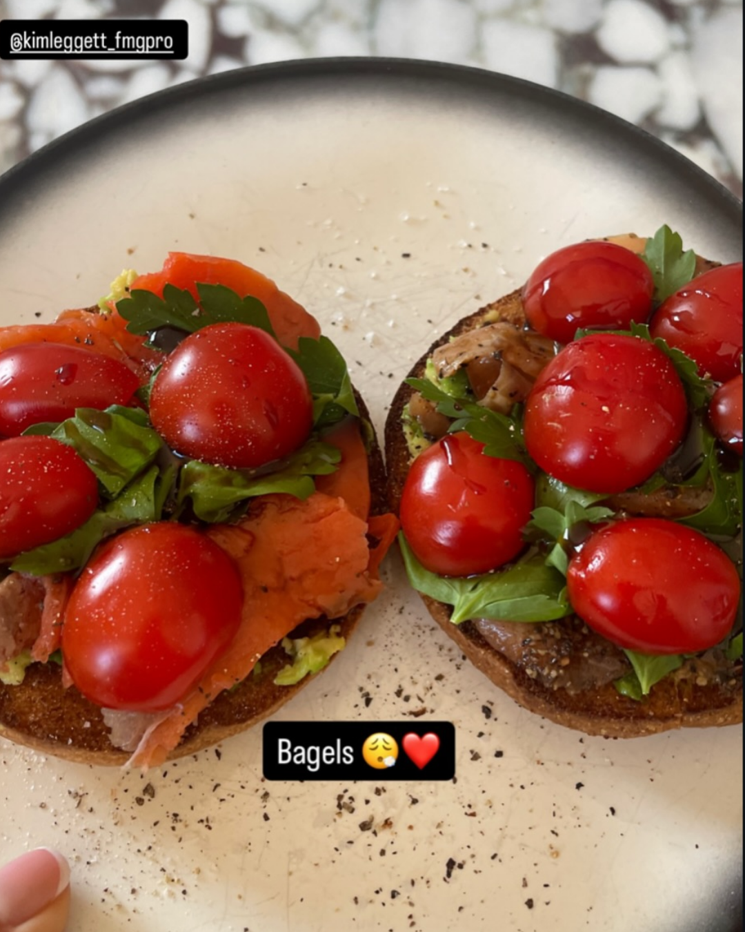 Two bagel halves topped with cherry tomatoes, fresh greens, and smoked salmon, served on a plate.