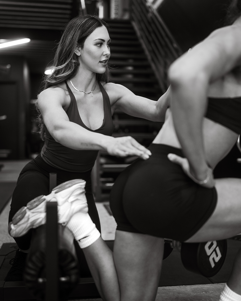 A woman in a gym coaching a woman doing squats with a barbell.