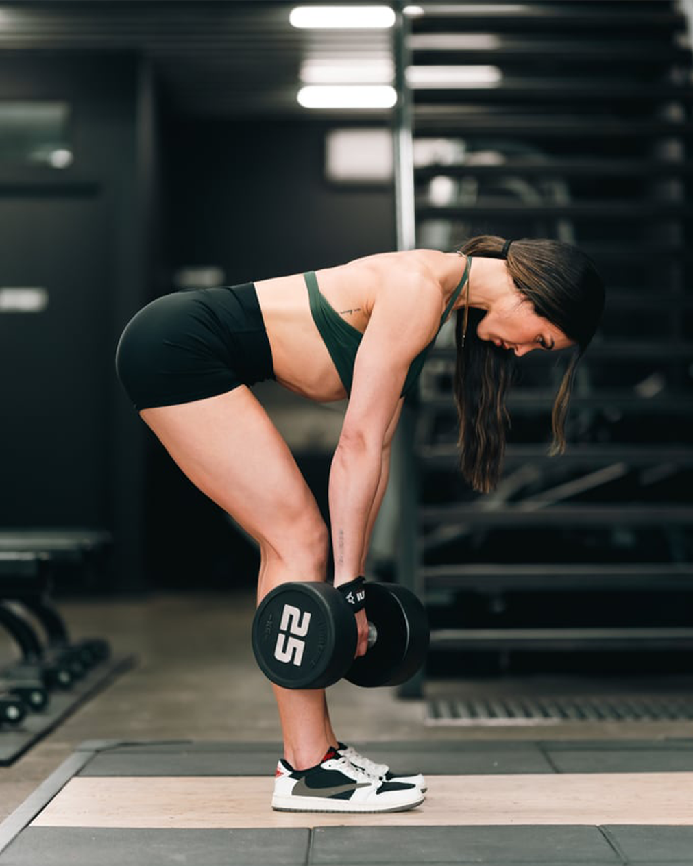 A woman in workout clothes performing a deadlift with dumbbells in a gym.