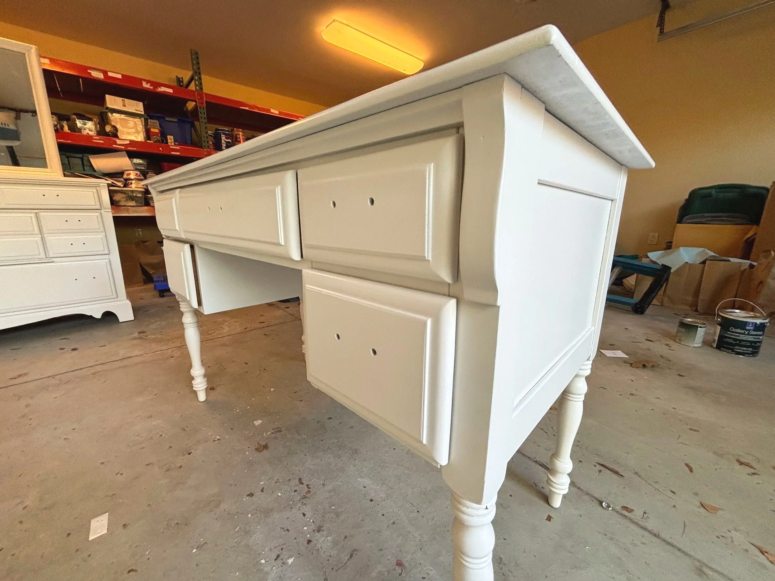 A white wooden desk with drawers in a storage or workshop area.