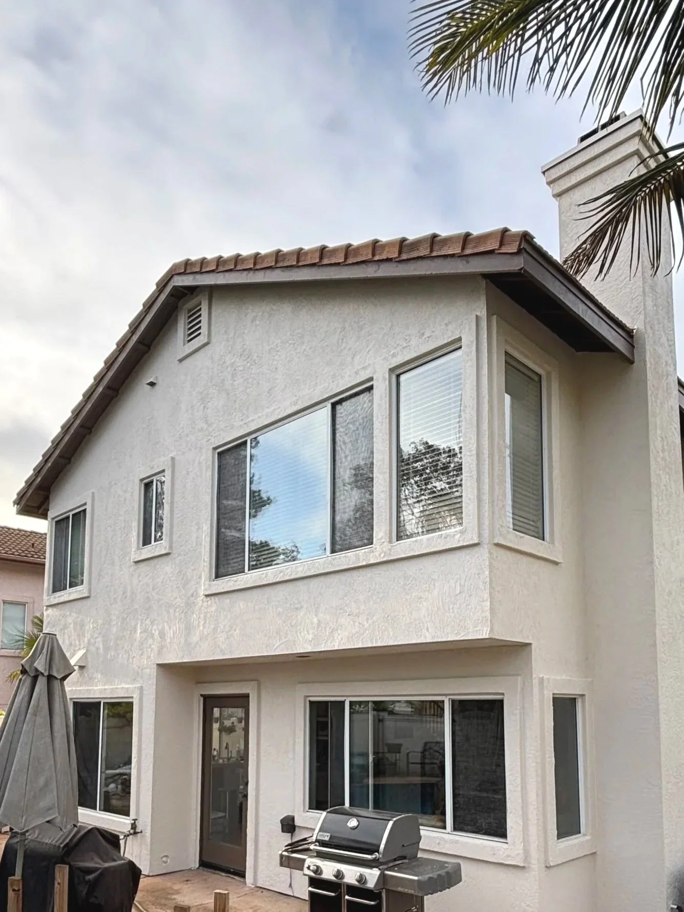 Rear view of a white two-story house with large windows, a barbecue grill, and an outdoor patio area.