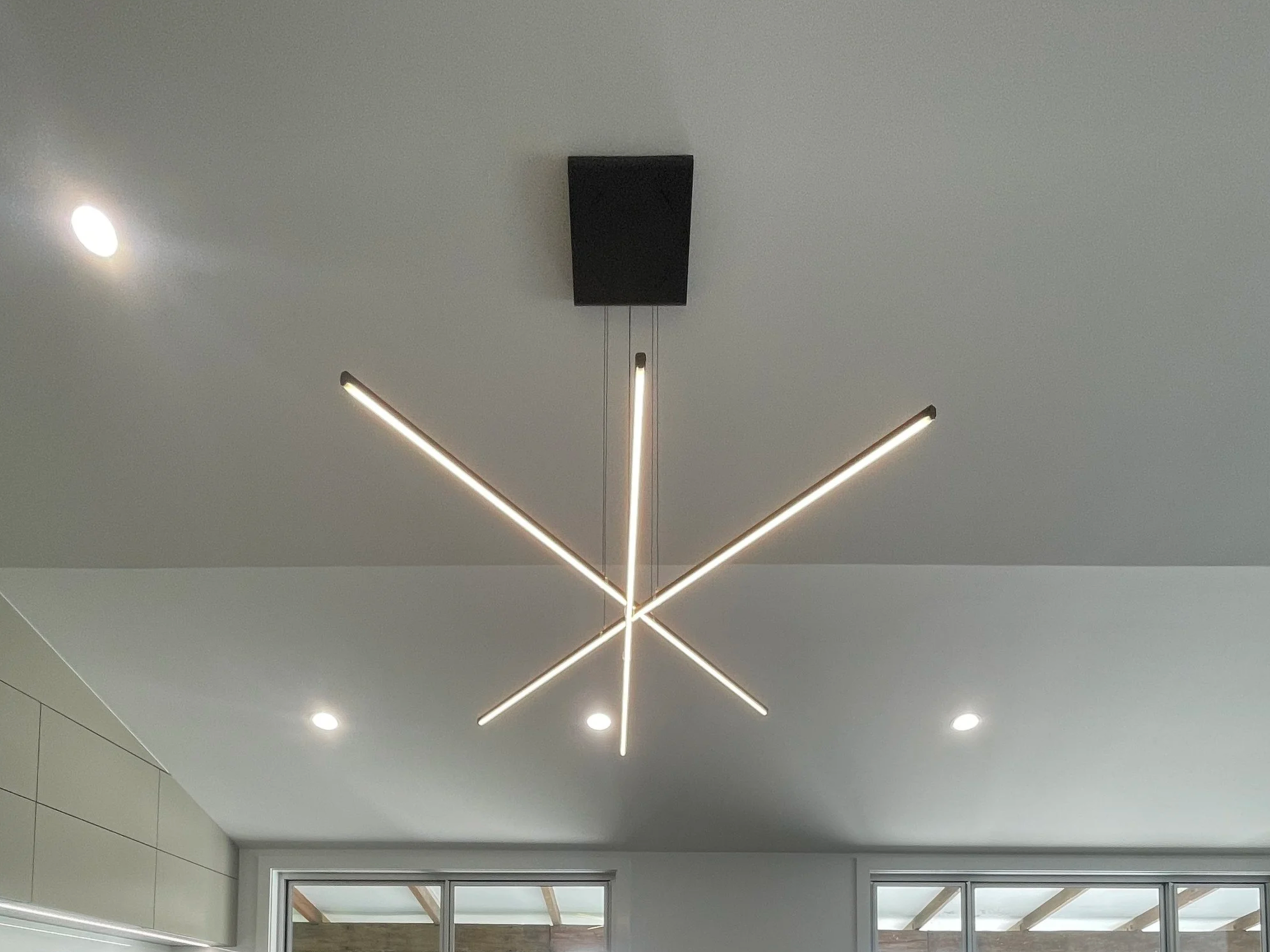 Modern geometric ceiling light fixture with LED strip lights and recessed ceiling lights in an indoor setting.