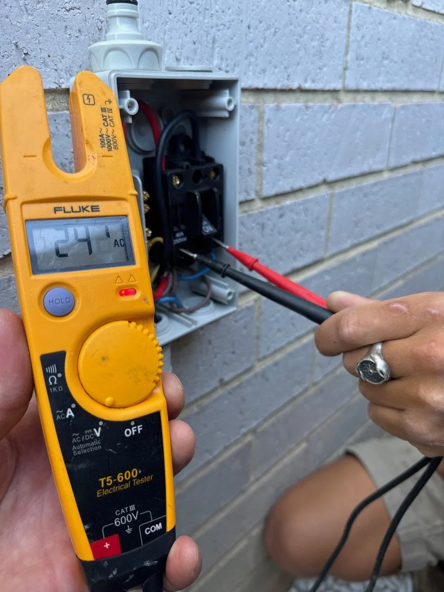 Person testing an electrical outlet with a multimeter. The multimeter displays a reading of 24.1 volts.