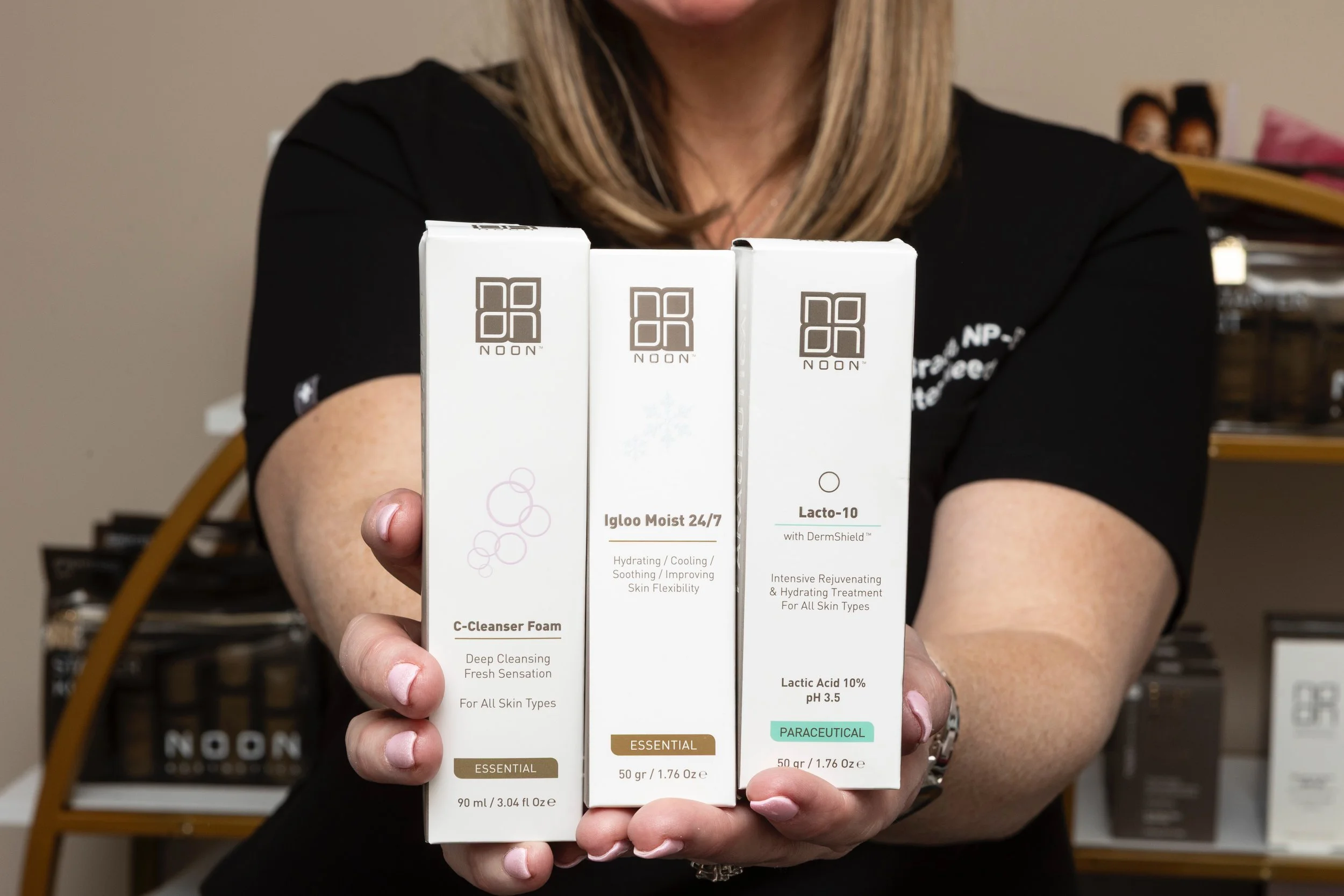Person holding three skincare product boxes from the brand NOON, with shelves of similar products in the background.