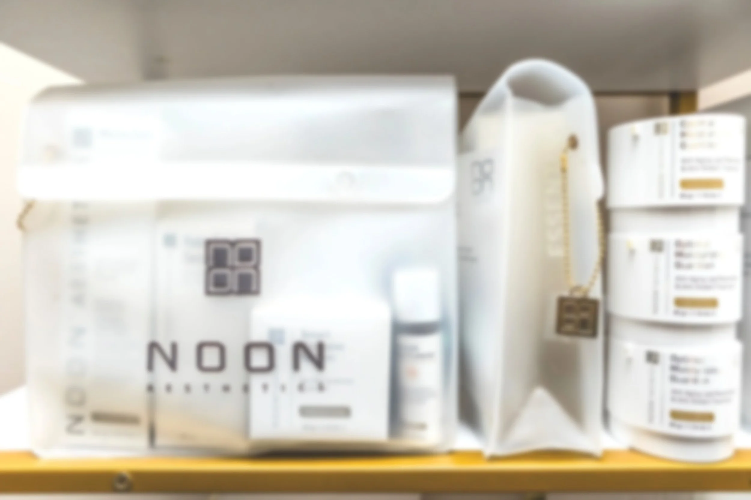 Pharmacy shelf with over-the-counter medication boxes and bottles, including a large silver box labeled 'NOON' and white bottles with labels.