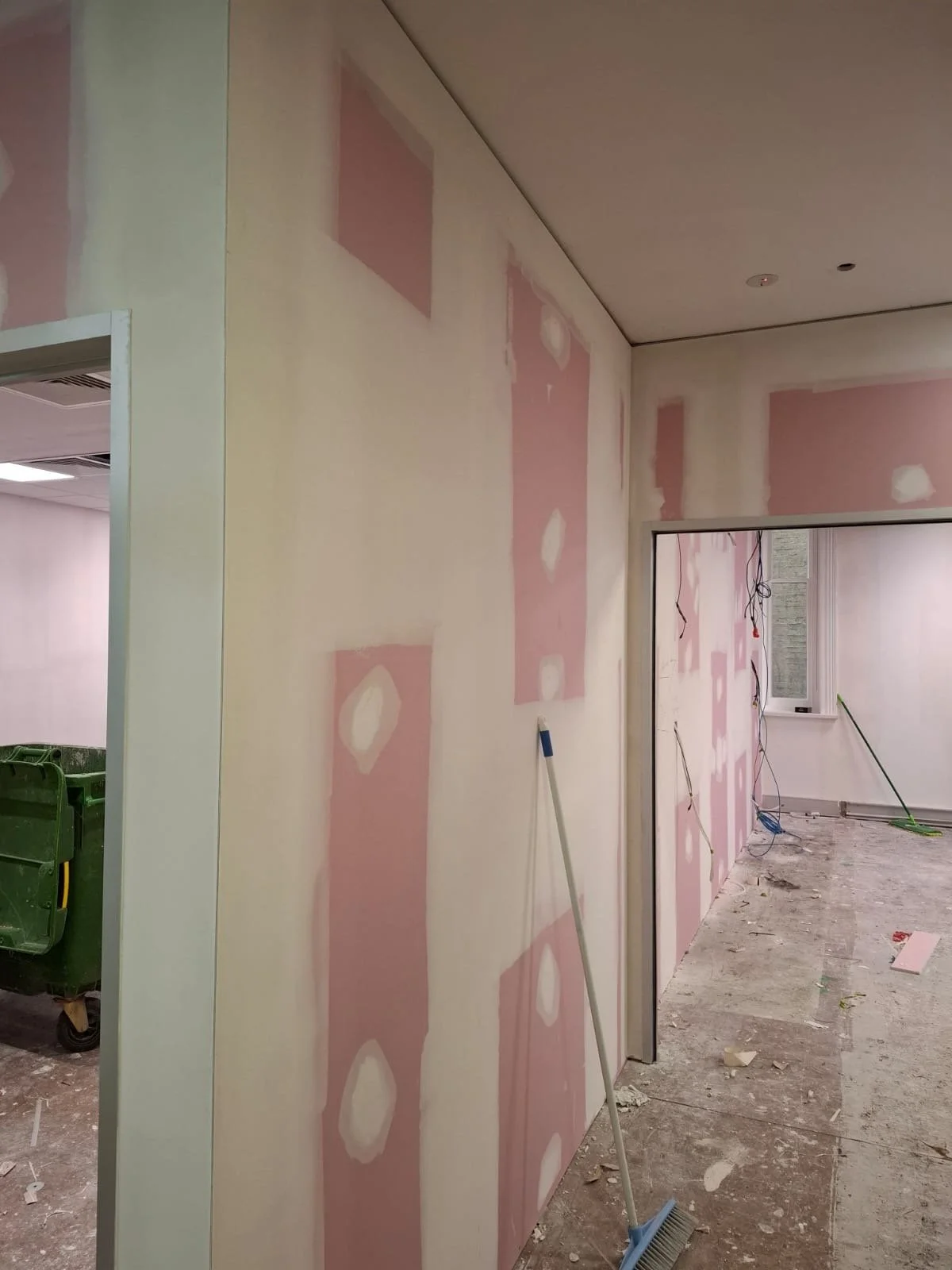 Interior under renovation with drywall installation and patchwork on pink drywall panels, construction tools, and debris on the floor.