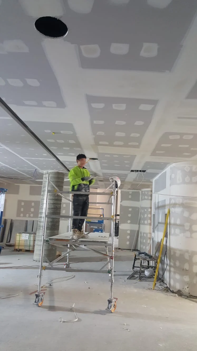 Construction worker standing on scaffolding working on ceiling drywall panels in an unfinished room