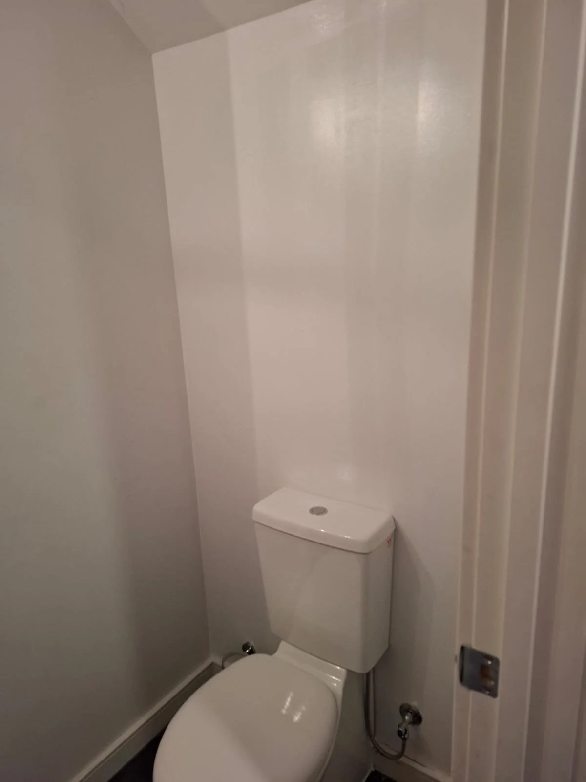 A small bathroom with a white toilet against the back wall, with plain white walls and a closed door on the right side.