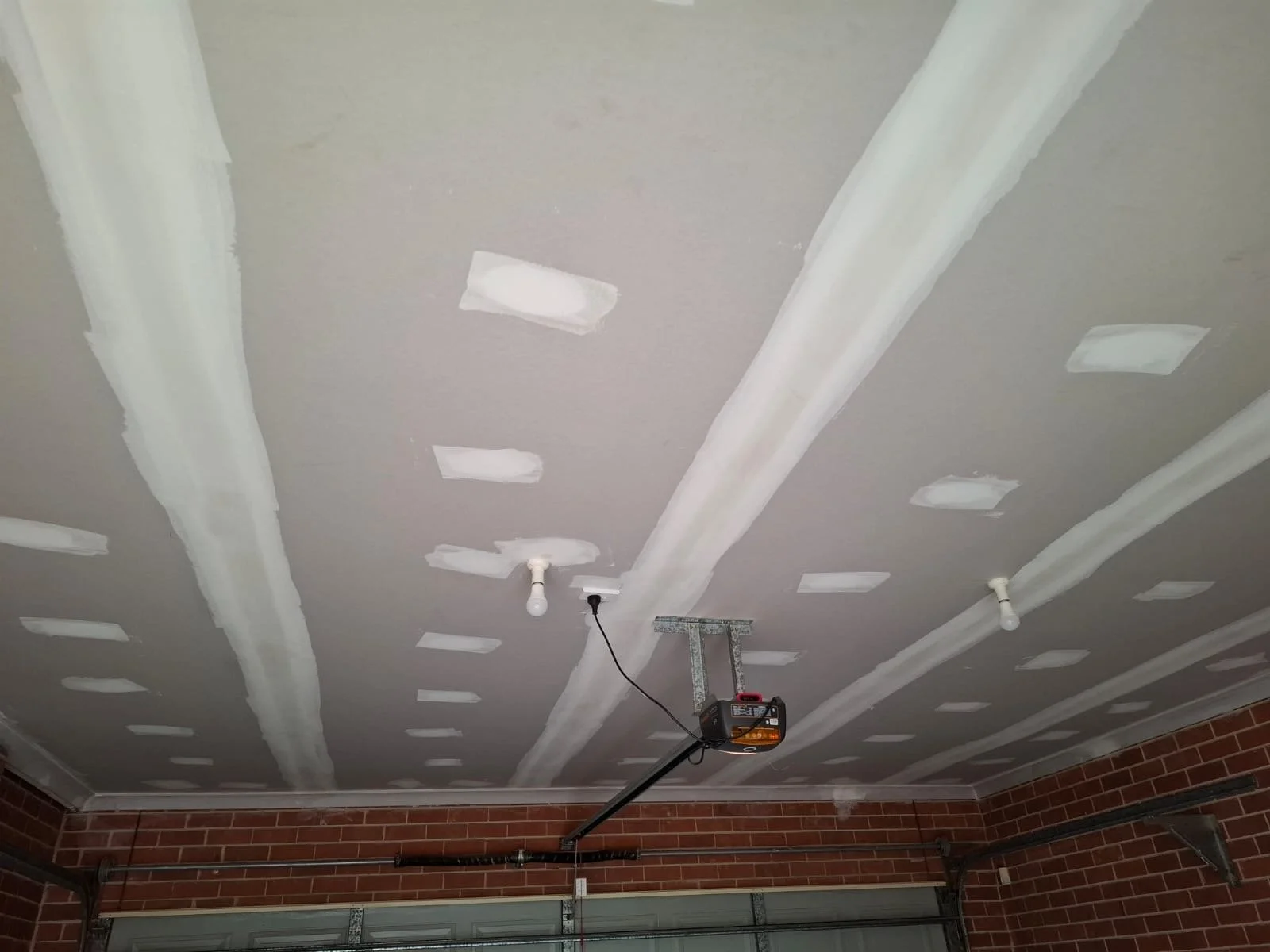 Garage ceiling with drywall patches and drywall compound, with two light fixtures and a garage door opener