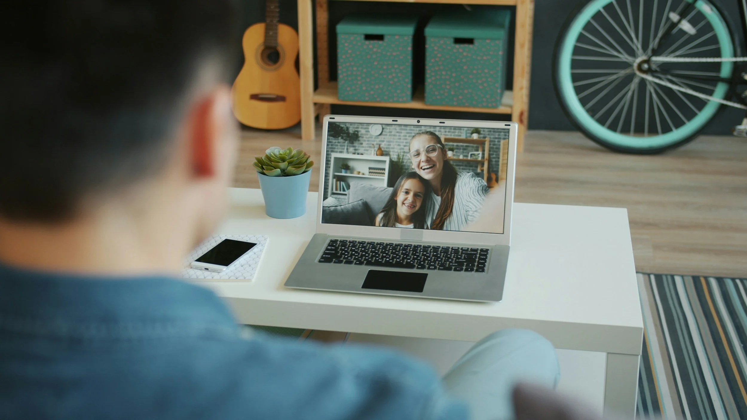 Person on video call with woman and girl on laptop screen in a cozy living room.