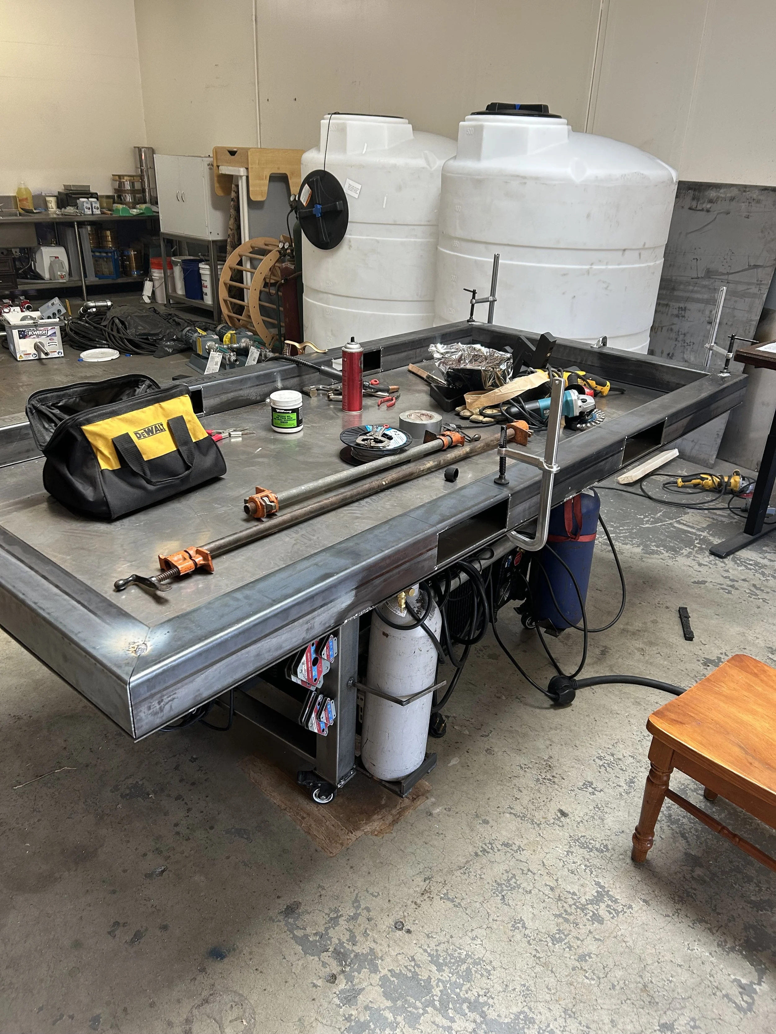 Workshop with metal table, tools, water tanks, and miscellaneous objects.