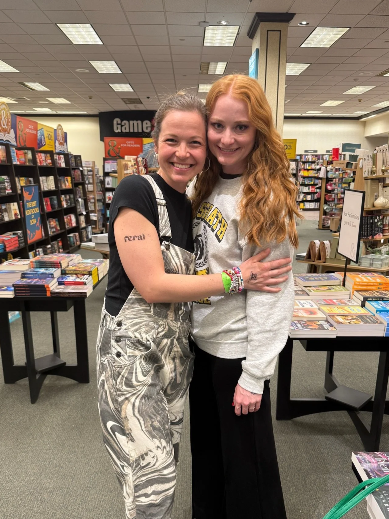 Two women hugging in a bookstore, surrounded by shelves of books and tables of books for sale.