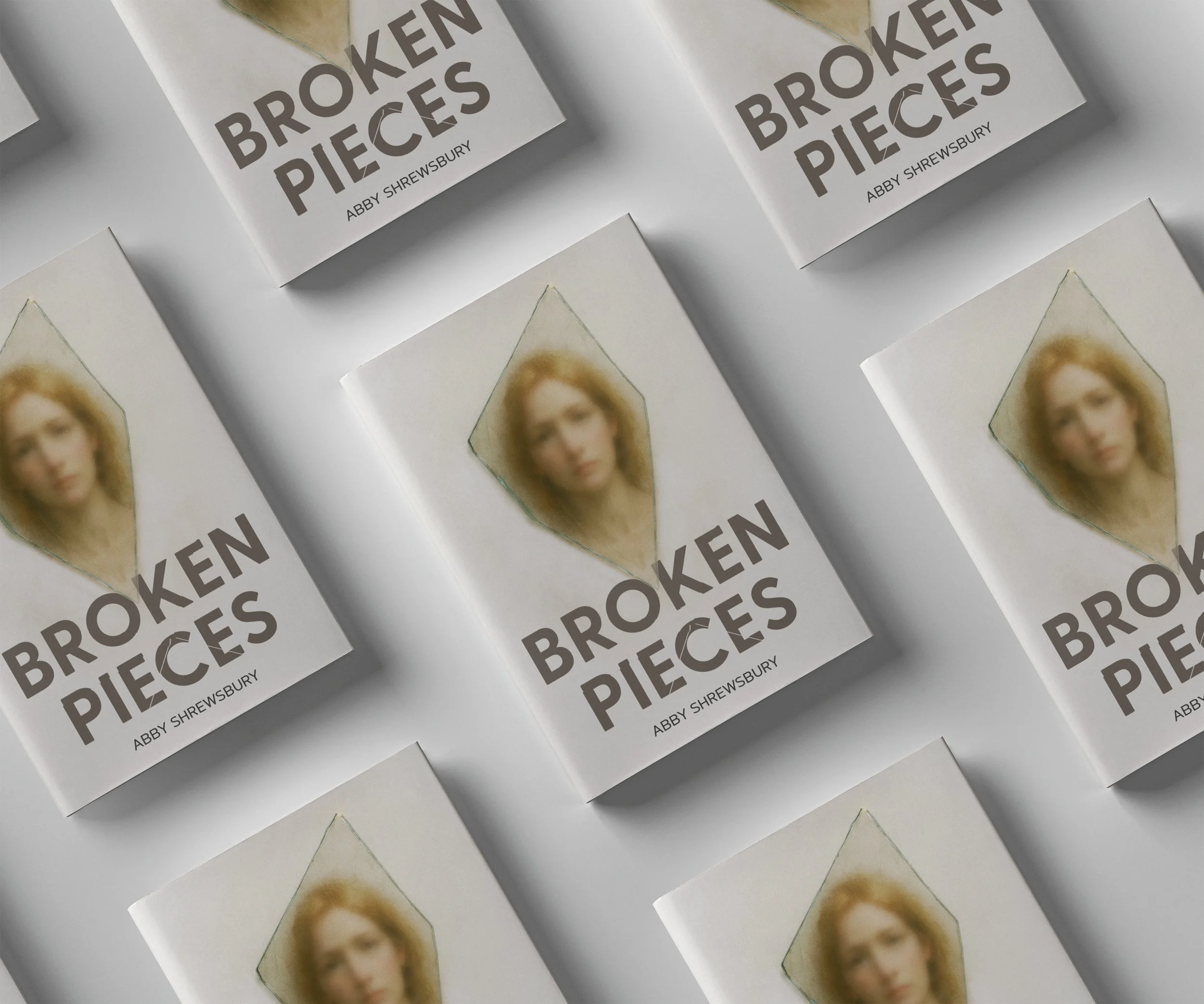 Multiple copies of a book titled "Broken Pieces" by Abby Shrewsbury, with a blurred portrait of a woman with blonde hair on the cover, arranged on a white surface.