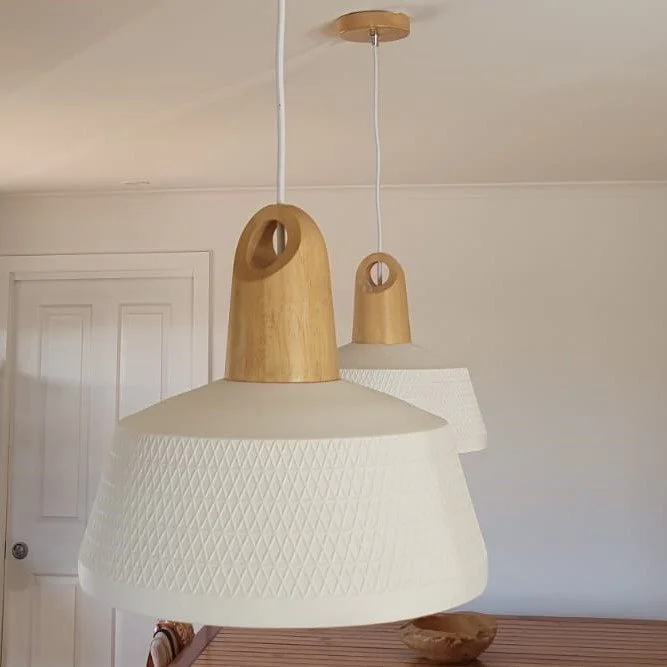 Two hanging pendant lights with wooden tops and white textured shades in a room with a white door and a wooden table.