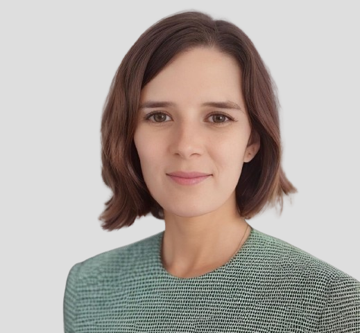 A portrait of a woman with shoulder-length brown hair, wearing a green patterned top, looking at the camera with a neutral expression, against a light gray background.