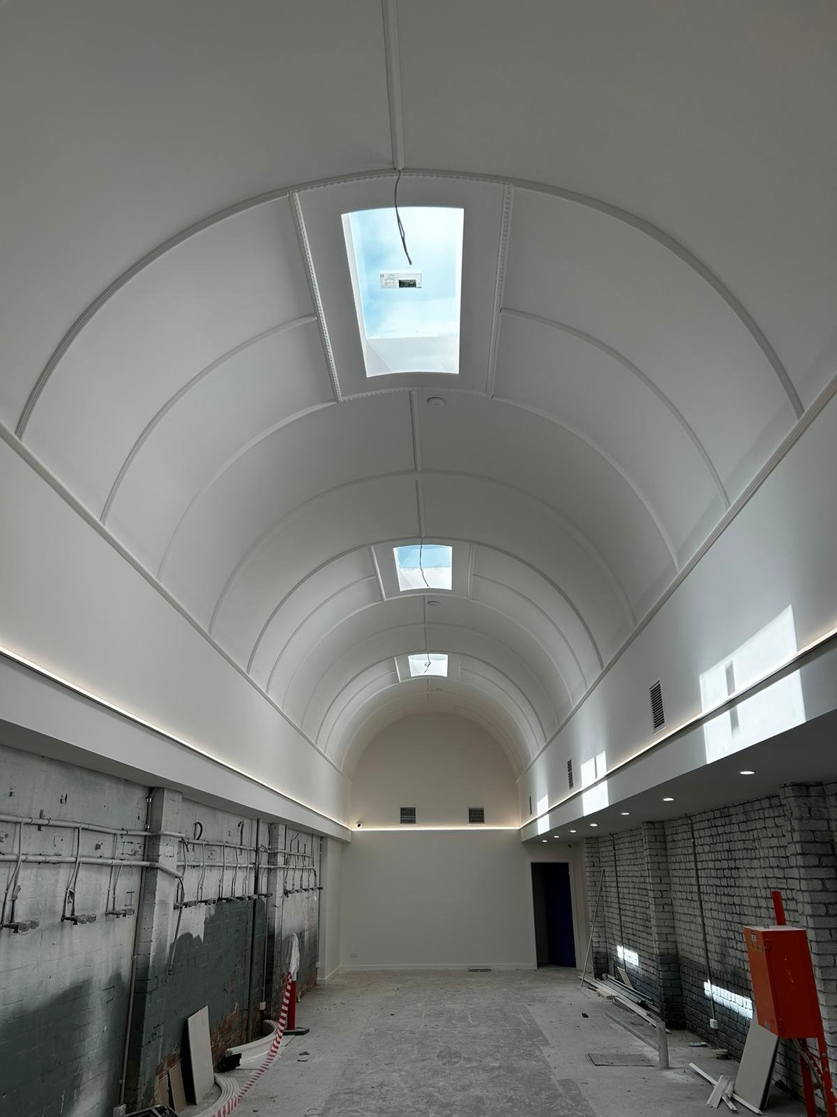 Interior of a building under construction with an arched ceiling, skylights, and construction materials on the floor, plastering and painting completed by JAYQ Plaster & Trades.