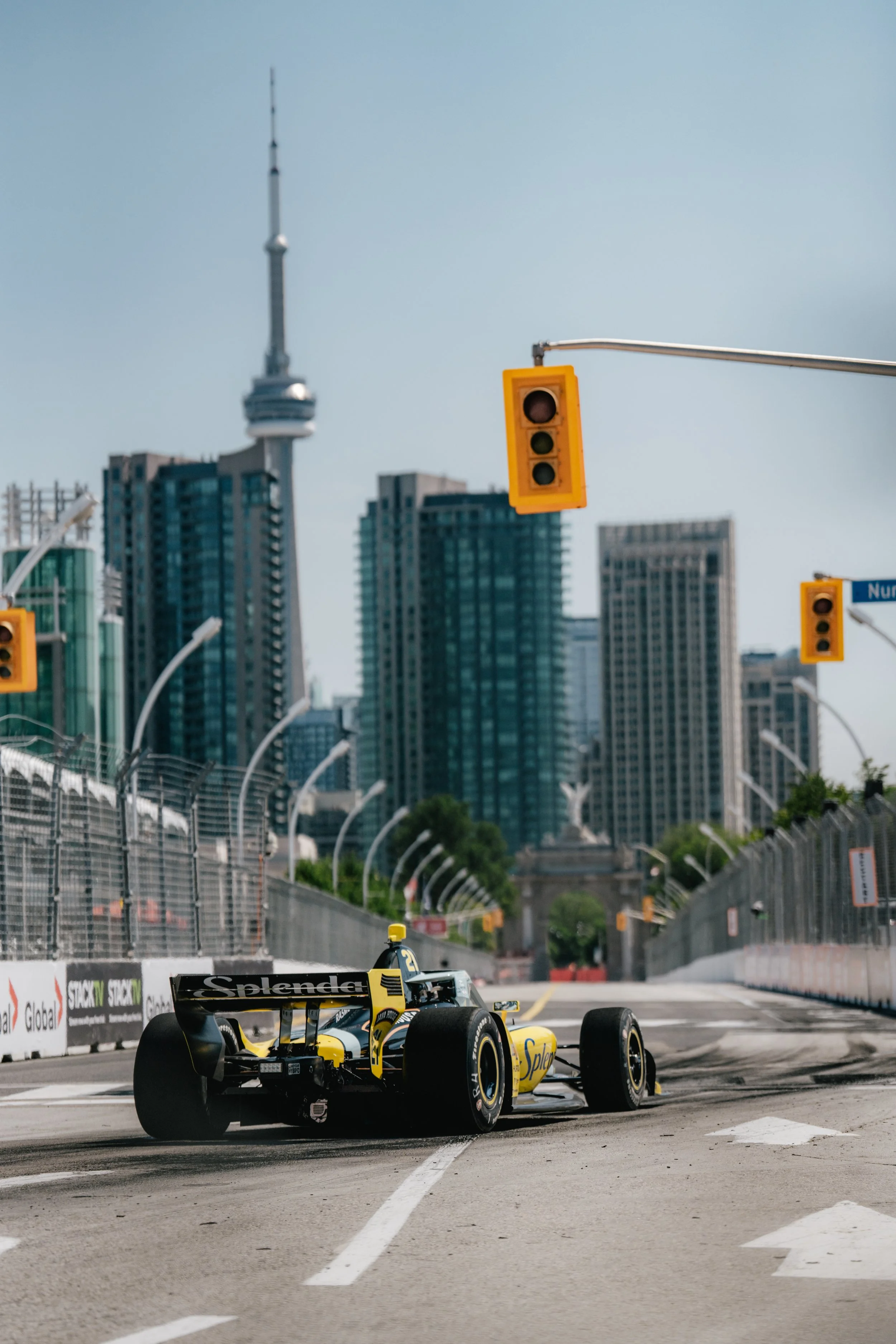 A yellow and black open-wheel race car on a city race track near traffic lights and city skyscrapers in the background, with tire marks on the asphalt.
