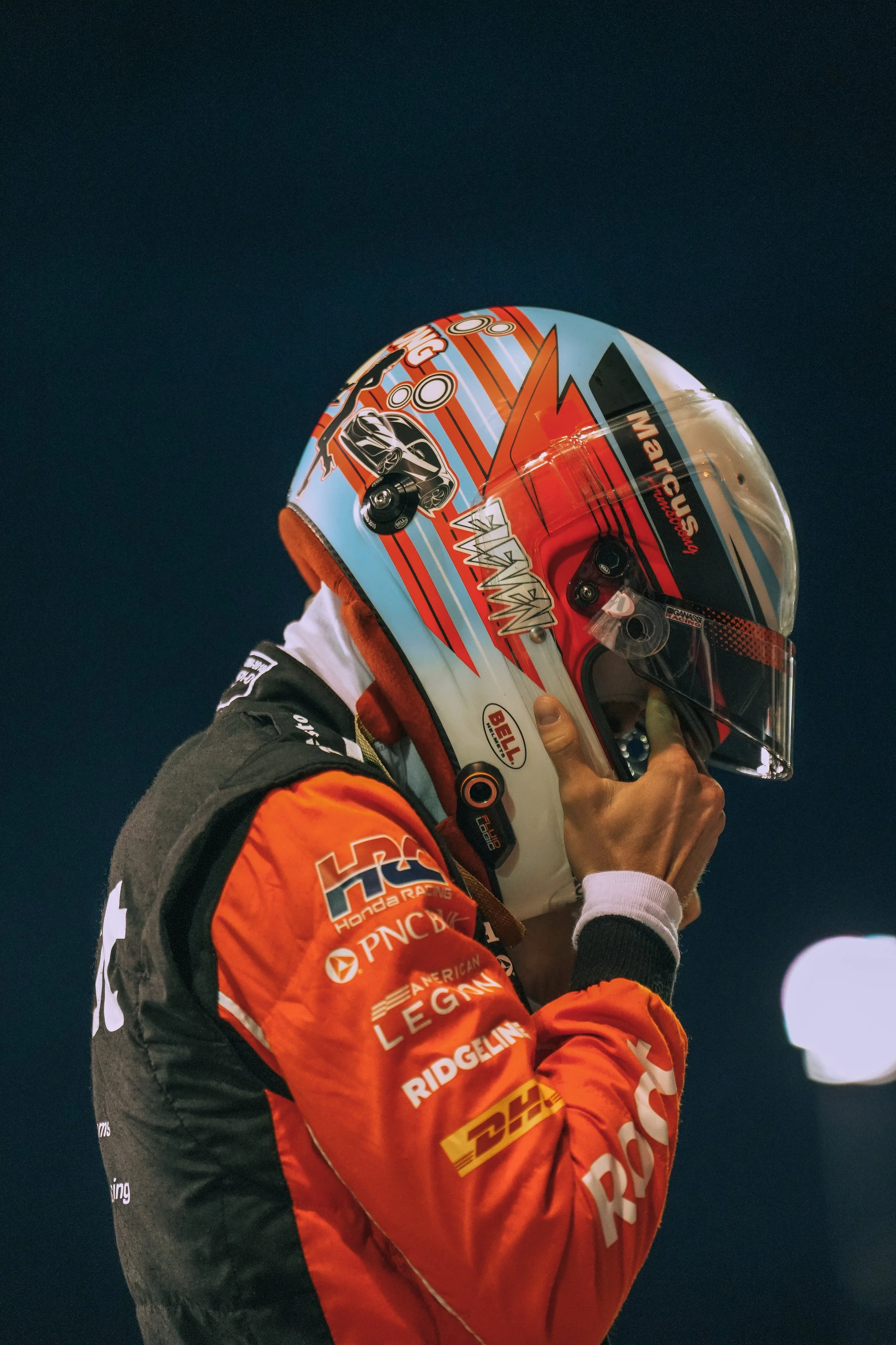 A race car driver in a red racing suit adjusting his helmet.