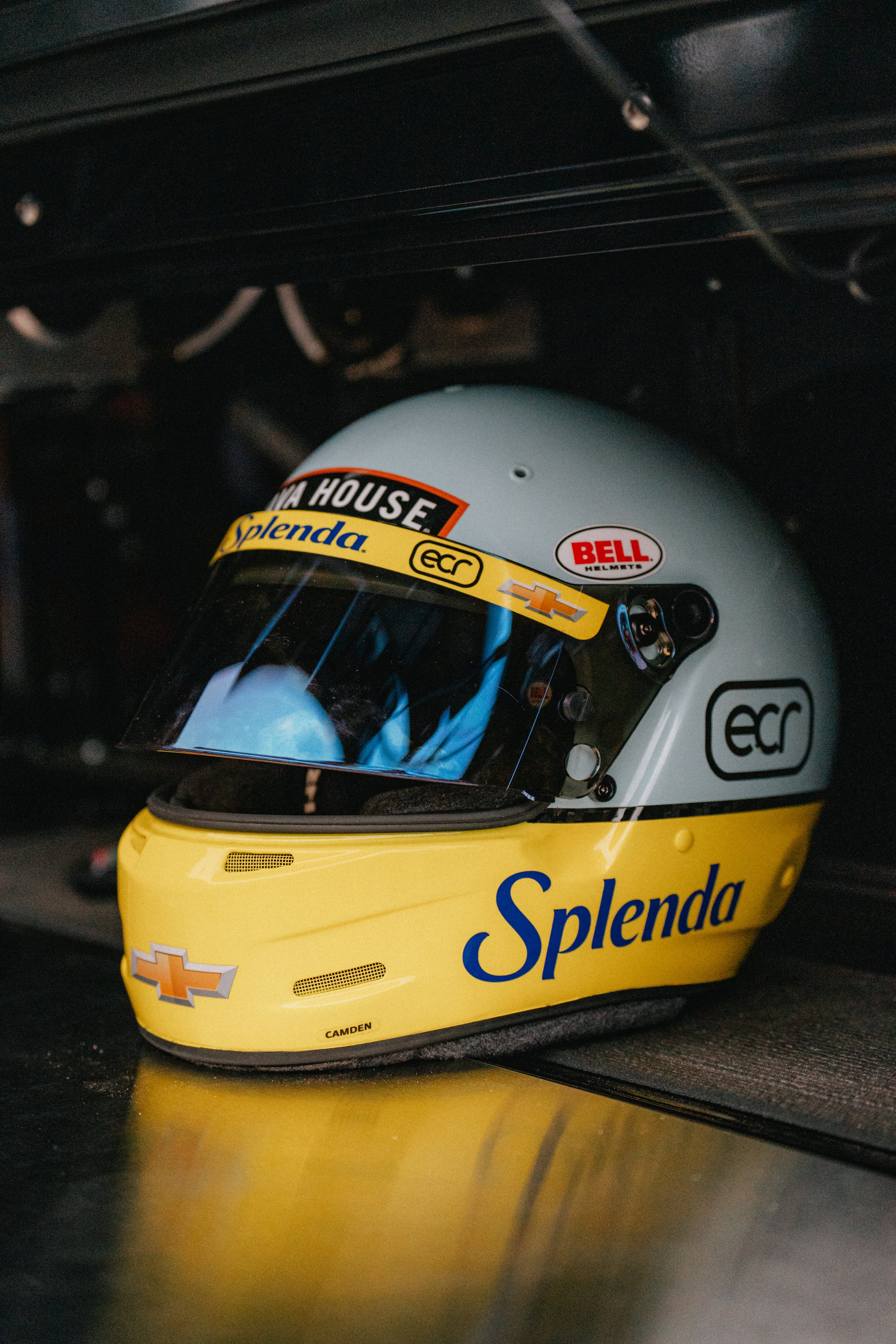 A racing helmet with a yellow and gray design placed on the floor inside a vehicle.