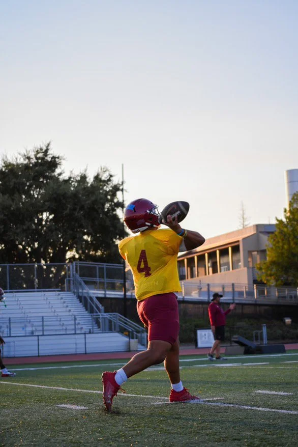 Football player in yellow jersey with number 4, red shorts, holding a football on a football field during practice or game.