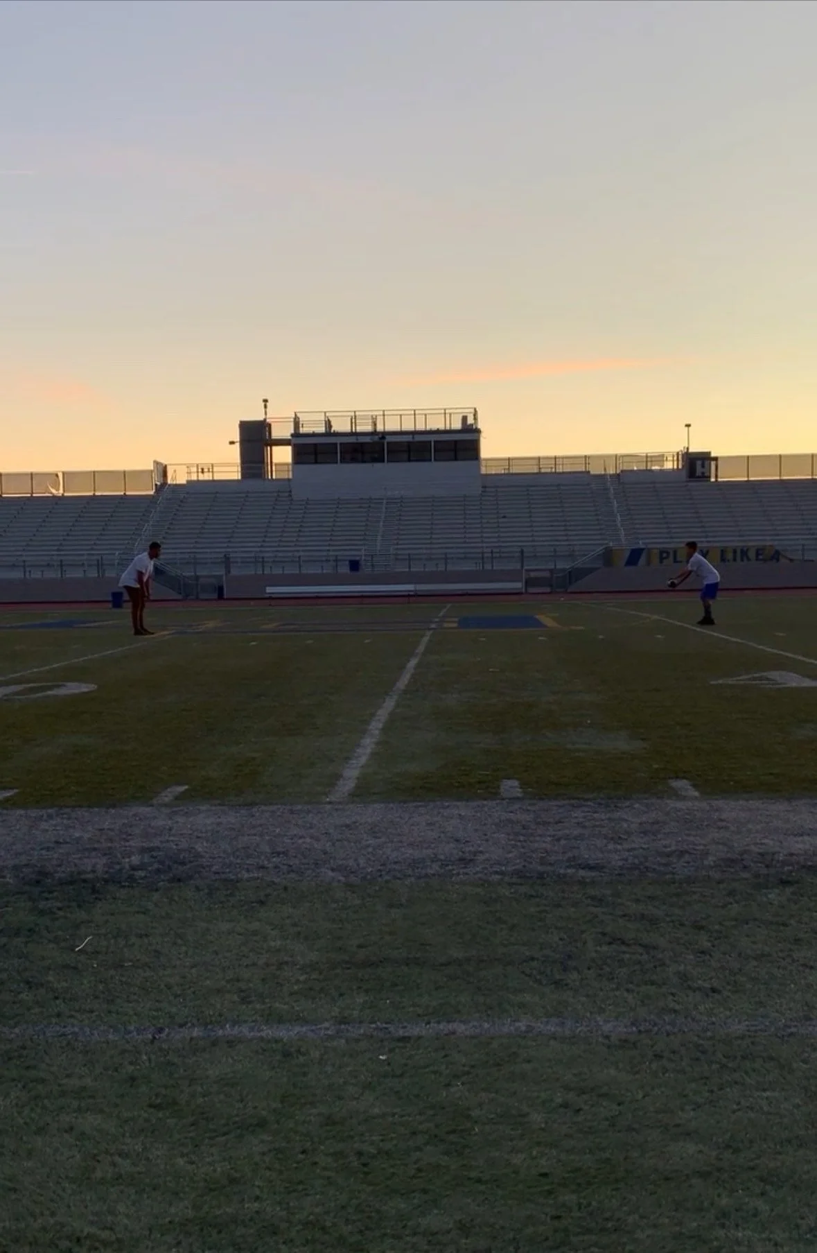 quarterback and quarterback coach preparing to play football on a field for the first time at sunset with empty bleachers in the background.