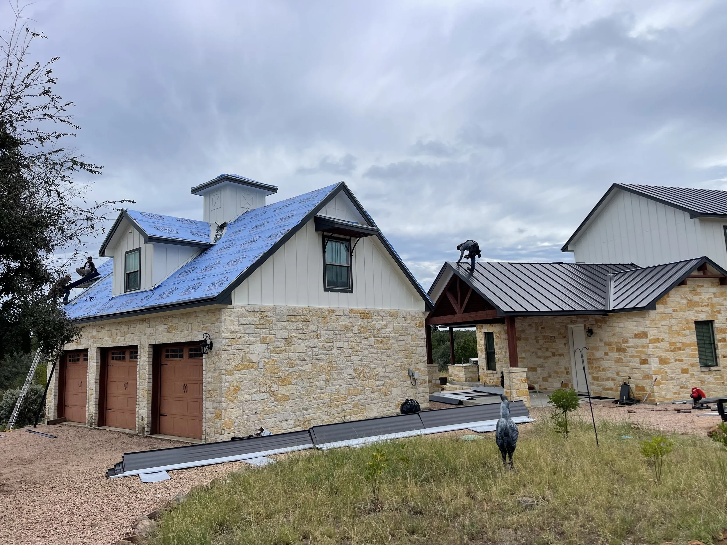 Professional roofing crew installing a standing seam metal roof on a stone masonry home in Central Texas for rainwater collection.