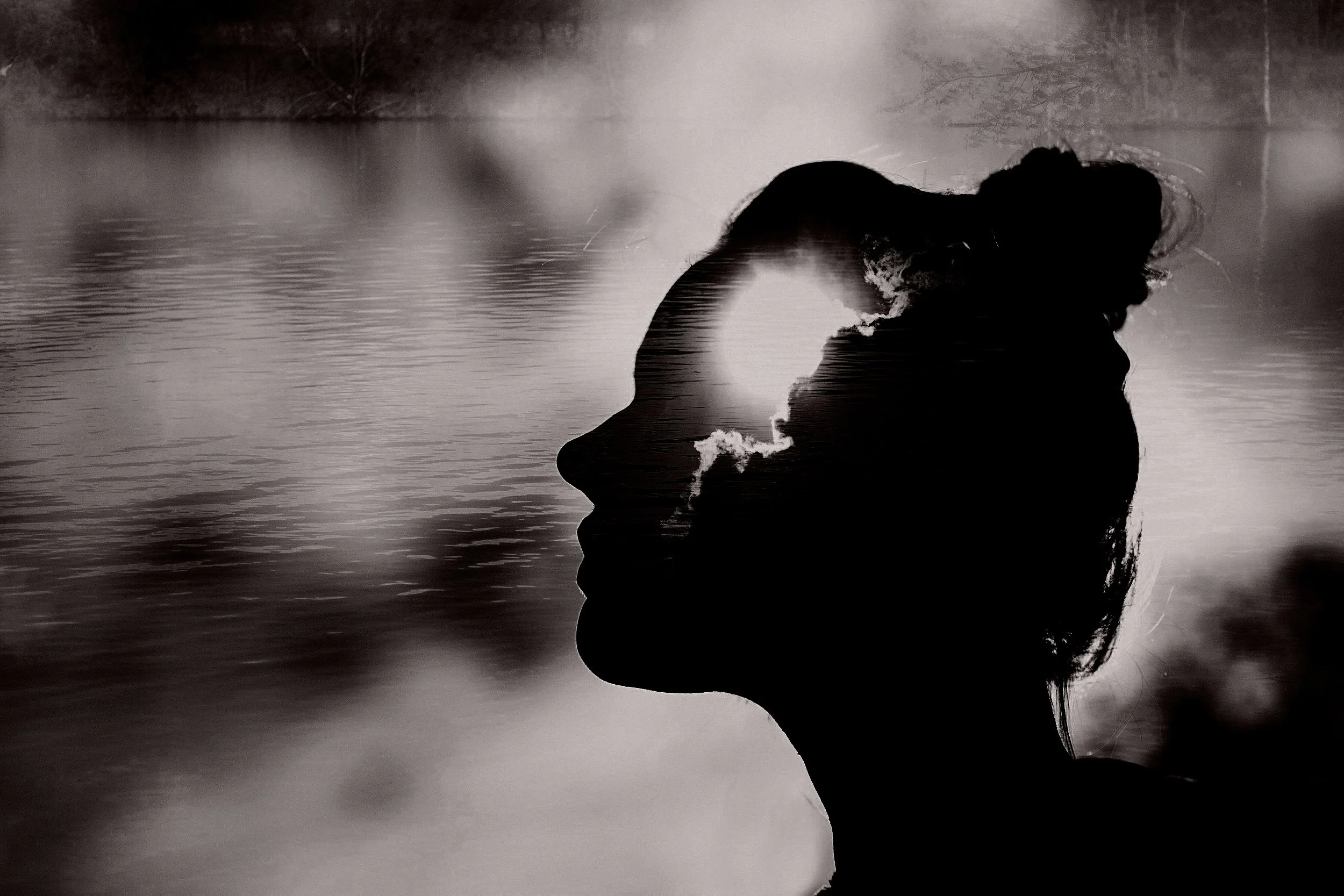 A double exposure black and white photo combining a woman's profile silhouette with a landscape of water and clouds, creating a surreal effect.