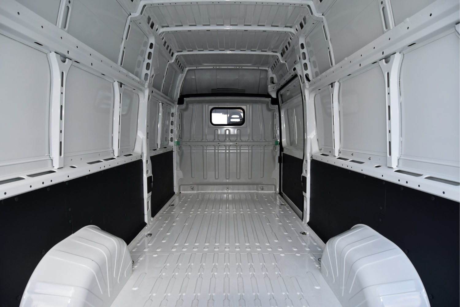 Empty white cargo van interior with metal walls and floor, small rear window, and black side panels.