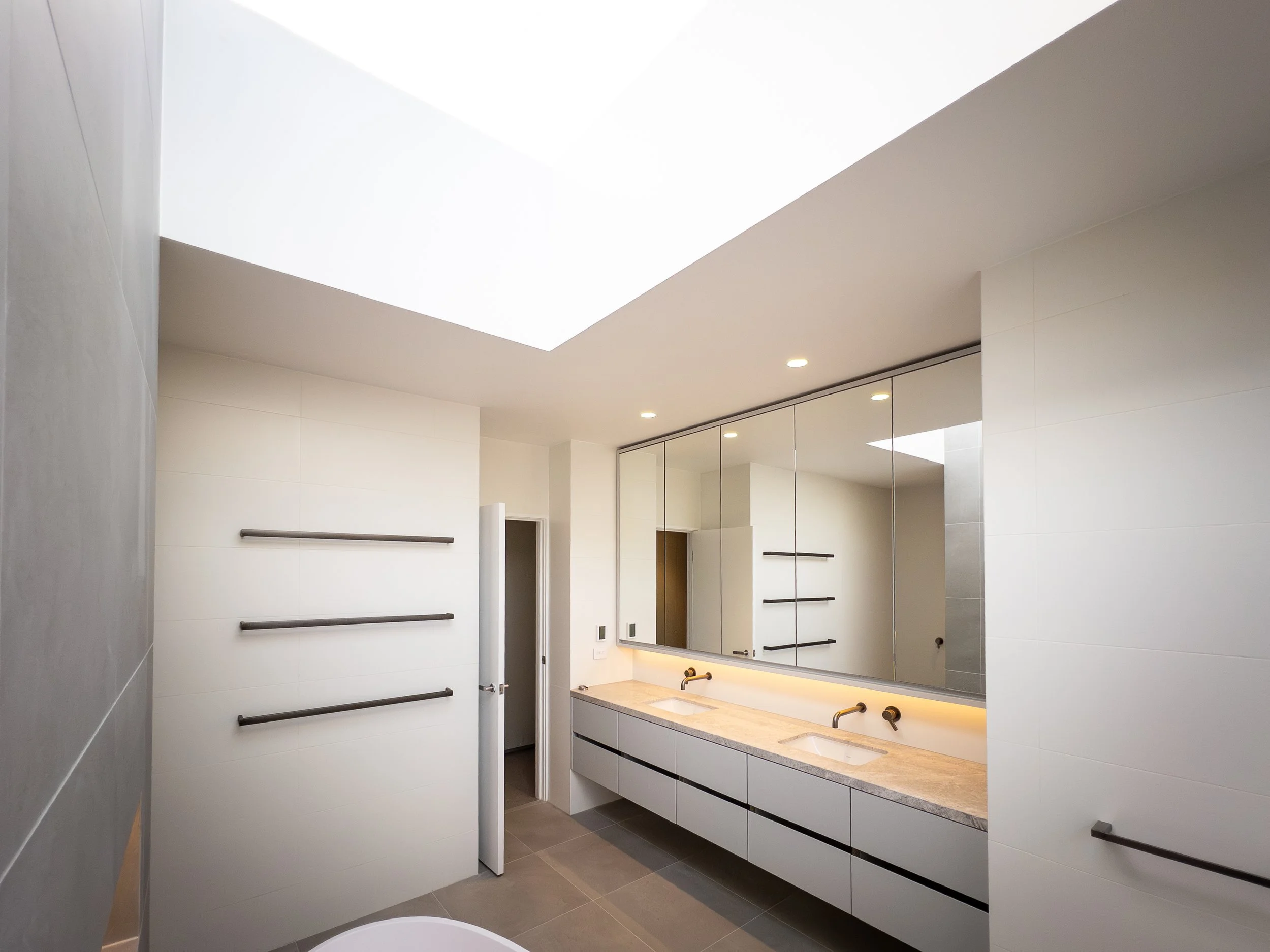 Modern bathroom with a double vanity, large mirror, and a skylight ceiling.