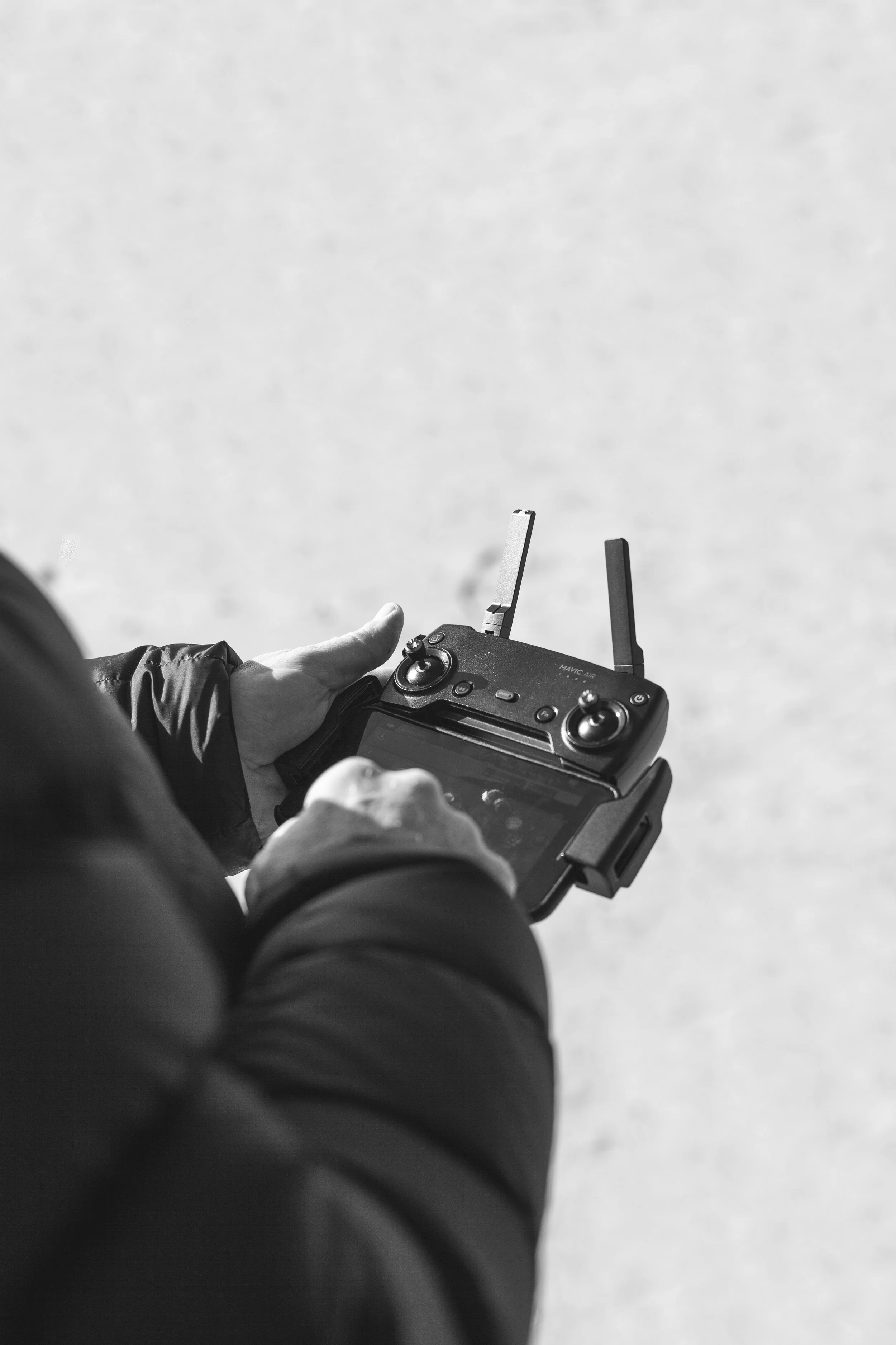 Person holding a drone remote controller with two antennas, outdoors on a plain surface.