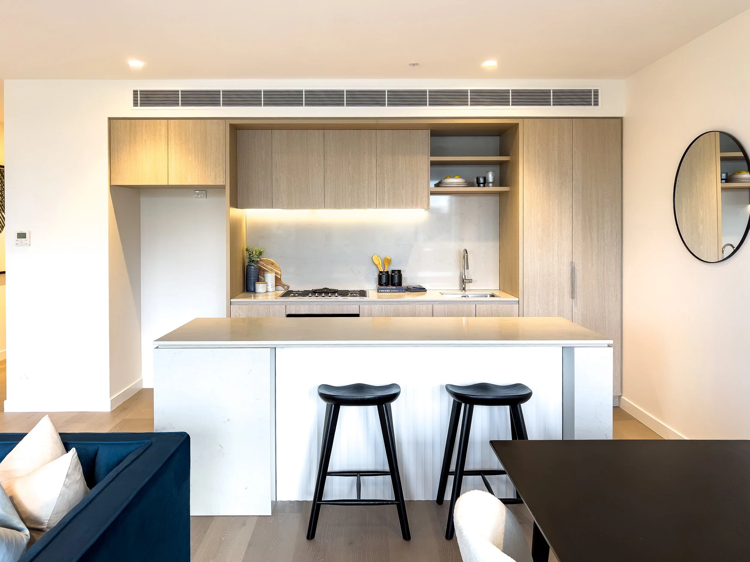 Modern kitchen with light wood cabinets, a white marble countertop, black bar stools, and minimal decor.