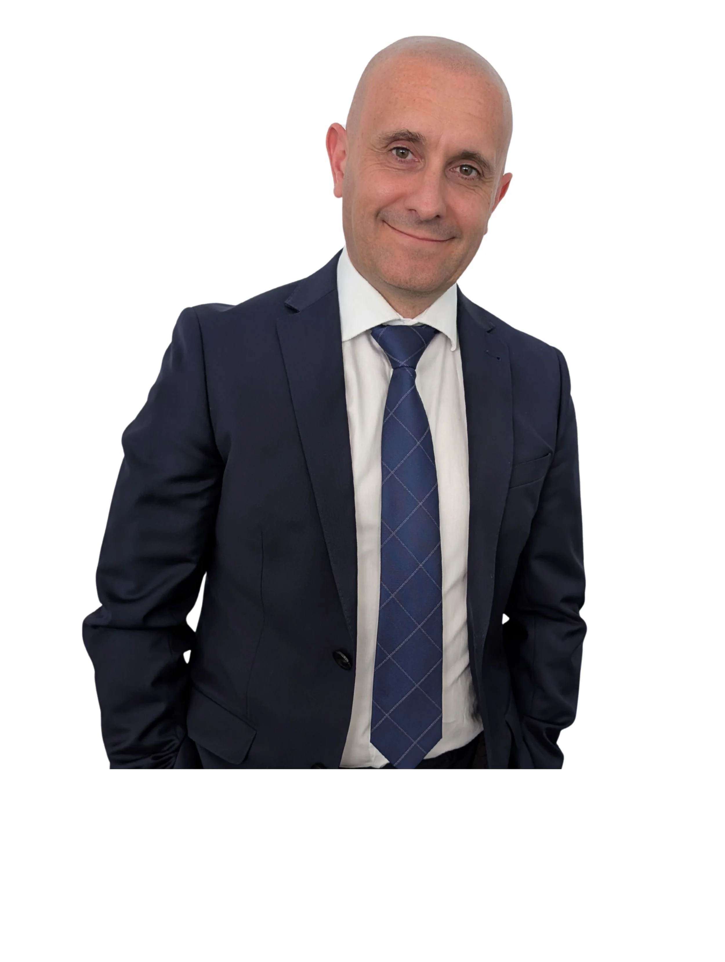 A bald man in a navy blue suit, white shirt, and blue tie, smiling with hands in pockets against a white background.