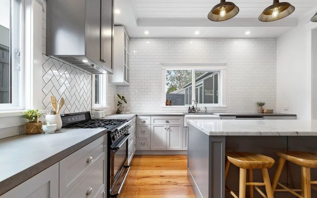 Classic kitchen with white cabinets, a gray island with wooden barstools, a stove, and a window above the sink.