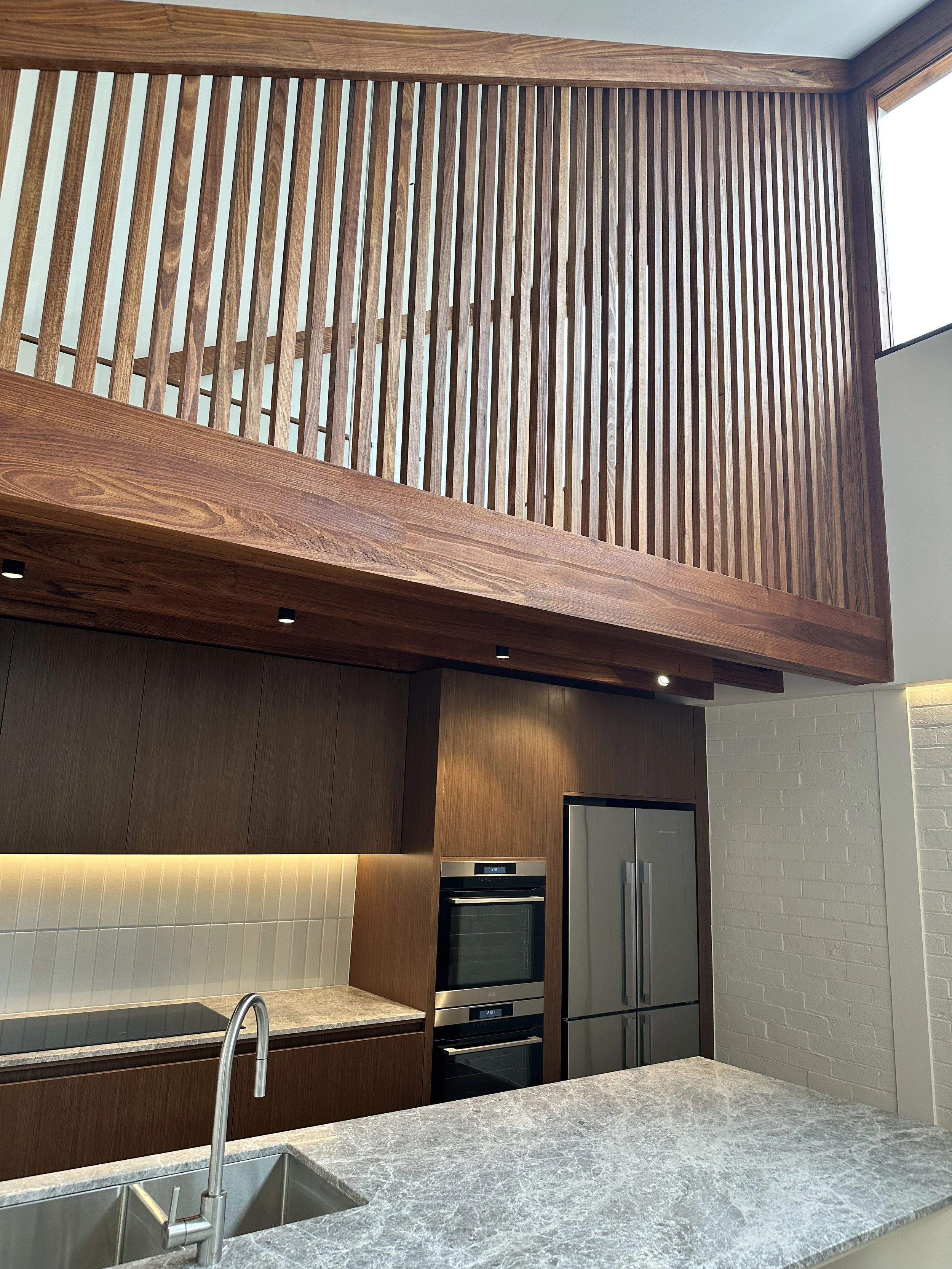 Modern kitchen with wooden cabinets, a marble countertop, and a stainless steel refrigerator, with a wooden railing overlooking an upper level.