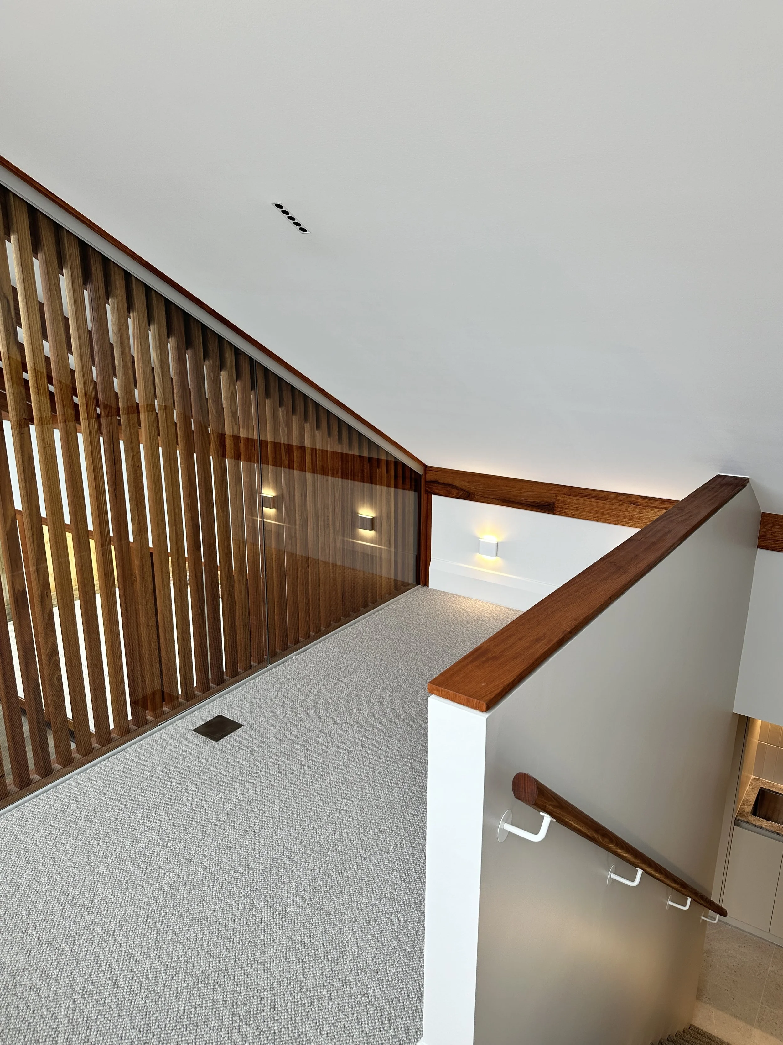 Interior view of a hallway with a staircase, wooden railing, and decorative wall lights.