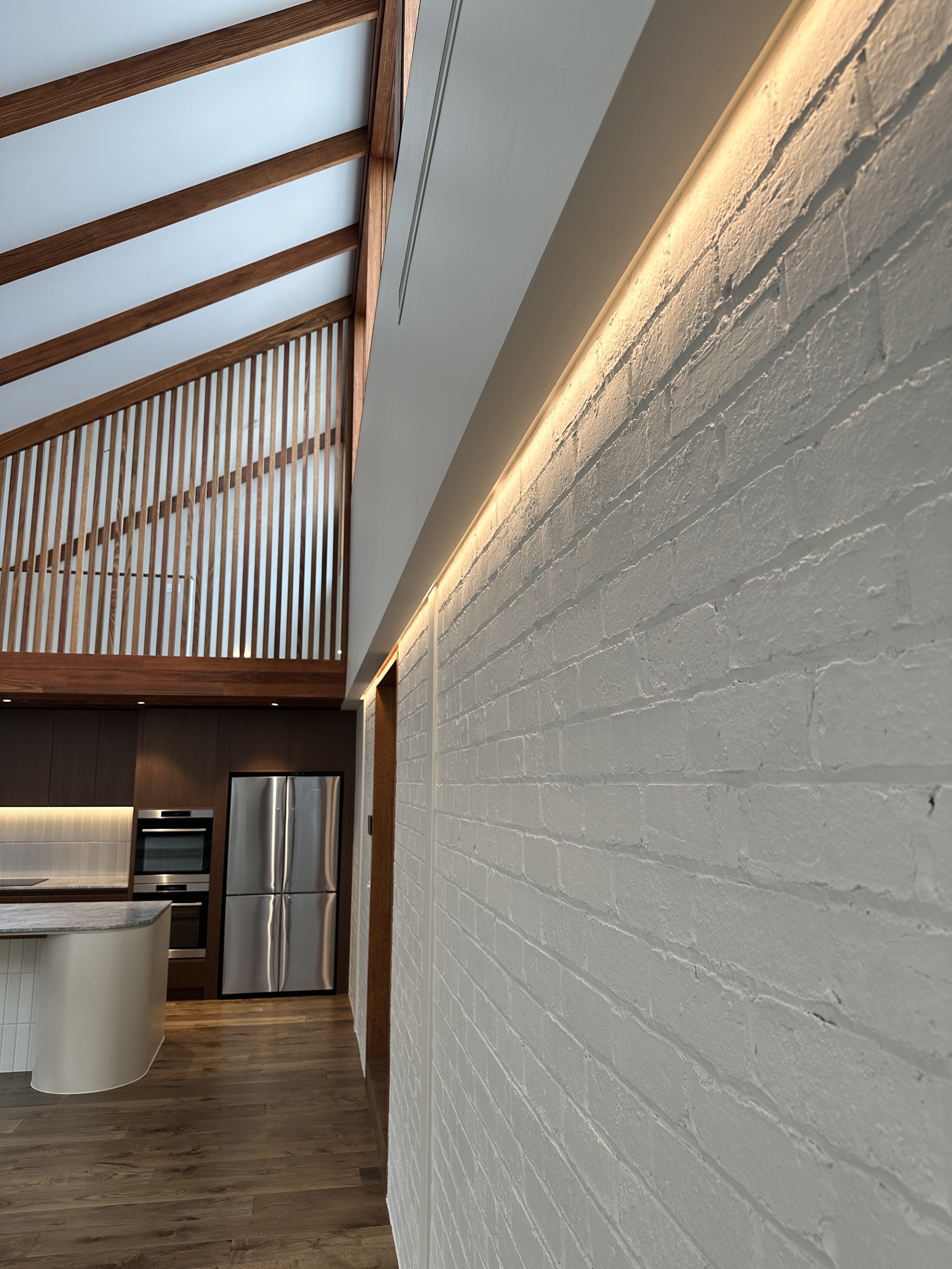 Interior view of a modern kitchen with white painted brick wall, wooden ceiling beams, and stainless steel refrigerator.