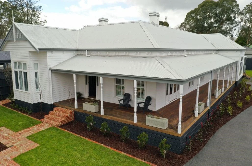 Large white house with a wraparound porch, metal roof, and a landscaped yard with a brick walkway.