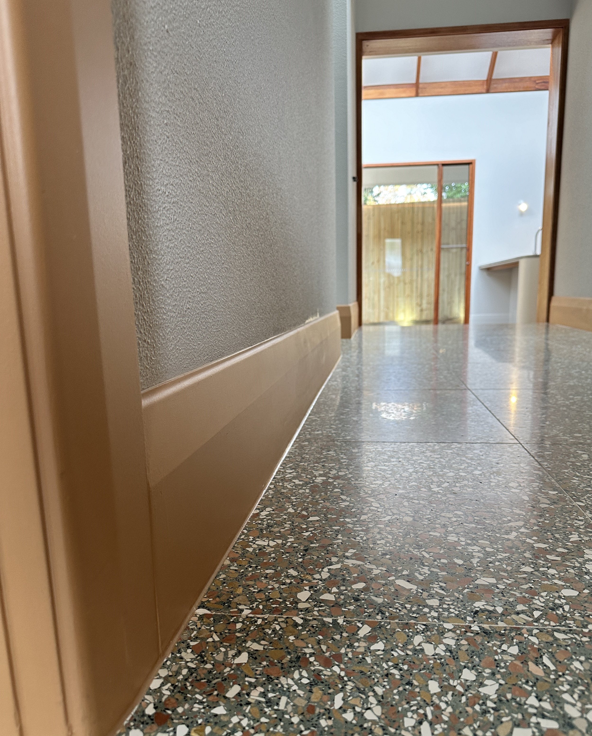 Indoor hallway view looking toward an entrance door with natural light, wooden trim, and terrazzo flooring.
