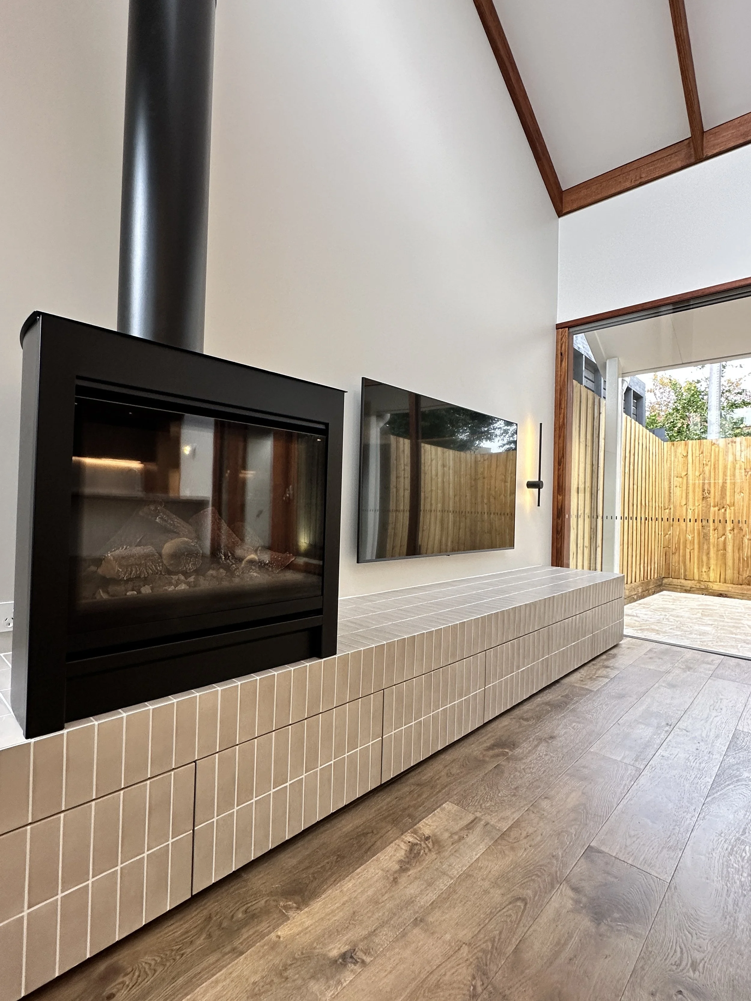 Modern living room with fireplace, wall-mounted TV, and sliding glass door leading outside.