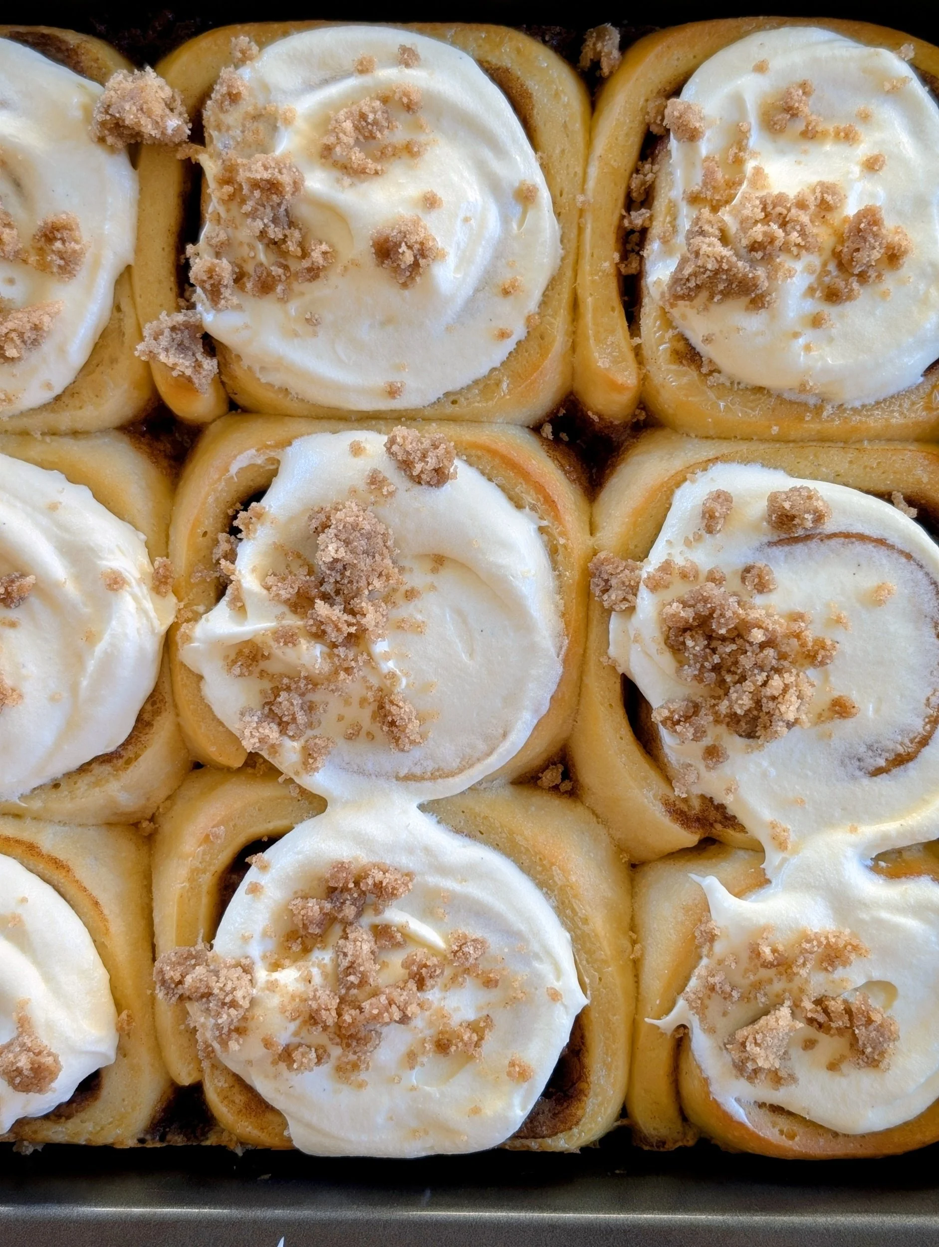 Close-up of cinnamon rolls topped with cream cheese frosting and crumbles.