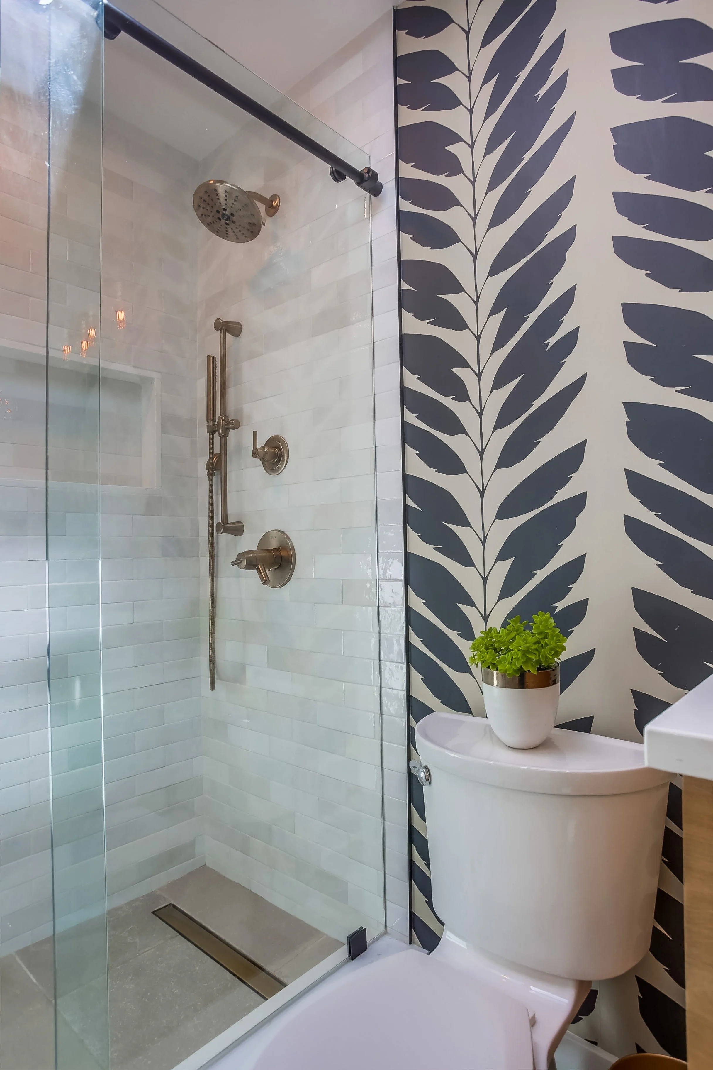 bathroom remodel with chloe white tile, brass fixtures, and patterned wallpaper accent wall in San Diego home