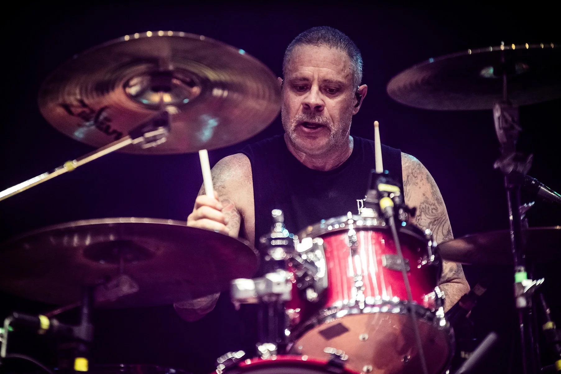 A male drummer performing on stage, playing a red drum set with cymbals.
