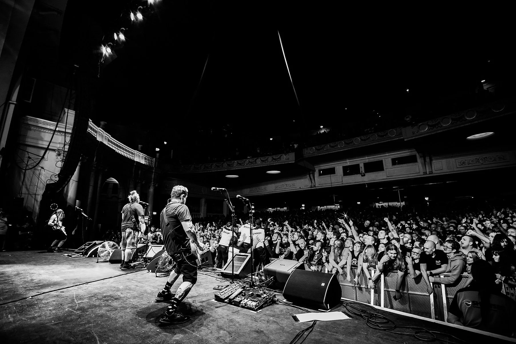 Black and white photo of a live concert with musicians performing on stage and an audience cheering.